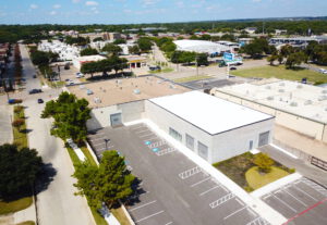 Aerial view of the backside of a light grey building with a white and brown roof and various different parking spaces