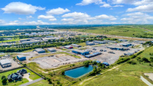 Zoomed-out aerial view of multiple warehouse buildings and blue shipping containers with views of the greenery and city