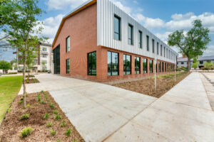 Exterior corner view of the backside of 133 Nursery Lane with a brick wall, large clear black windows, and tin siding